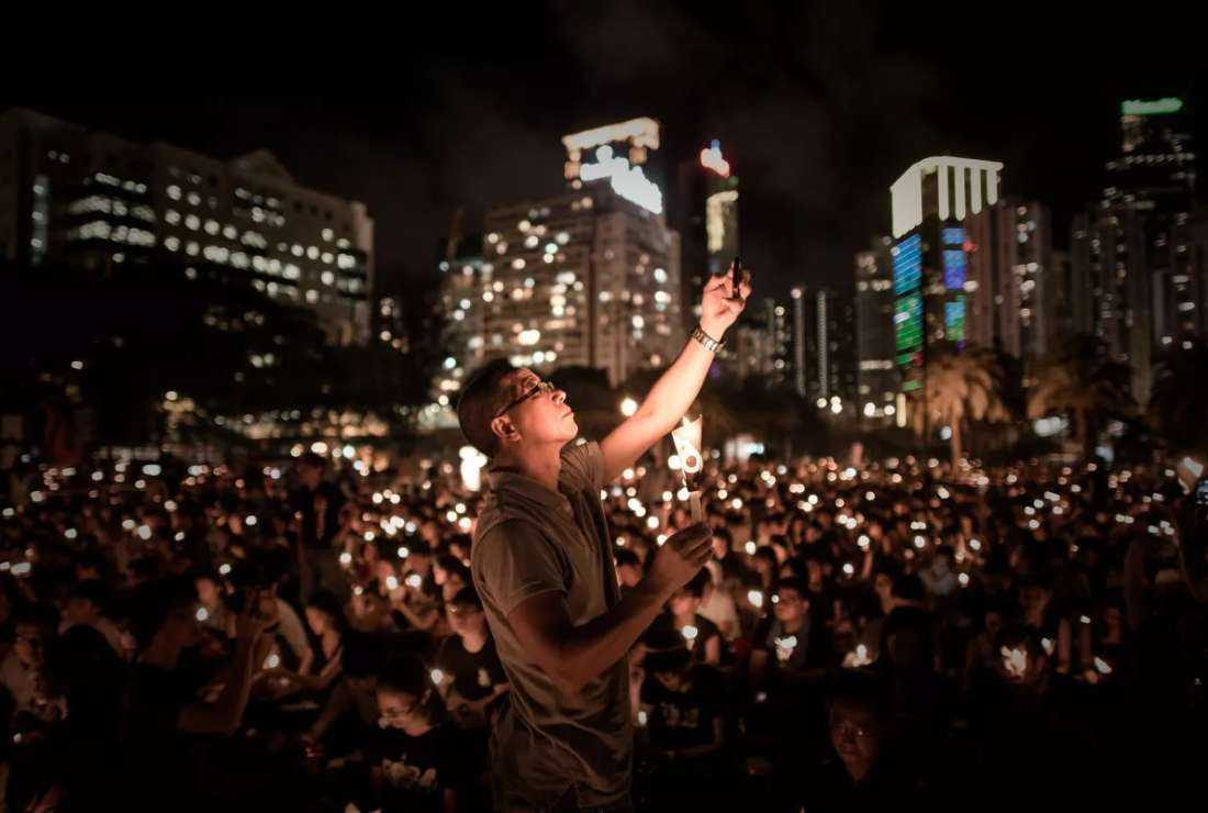 A man takes a picture with his phone as others hold candles at a vigil in Hong Kong to commemorate the 25th anniversary of the Tiananmen Square massacre in Beijing, in 2014