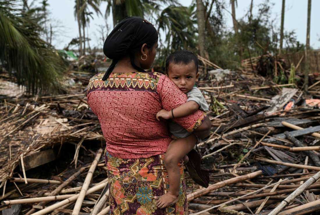 A Rohingya woman carries her baby next to her destroyed house at Basara refugee camp in Sittwe on May 16, after cyclone Mocha made landfall.